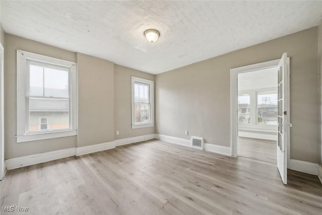 spare room featuring a textured ceiling and light hardwood / wood-style floors