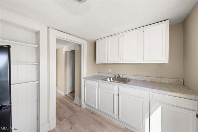 kitchen featuring light hardwood / wood-style flooring, sink, white cabinetry, a textured ceiling, and stainless steel fridge