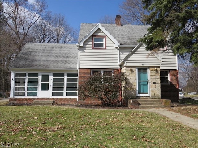 view of front facade featuring entry steps, a shingled roof, a chimney, and a front lawn