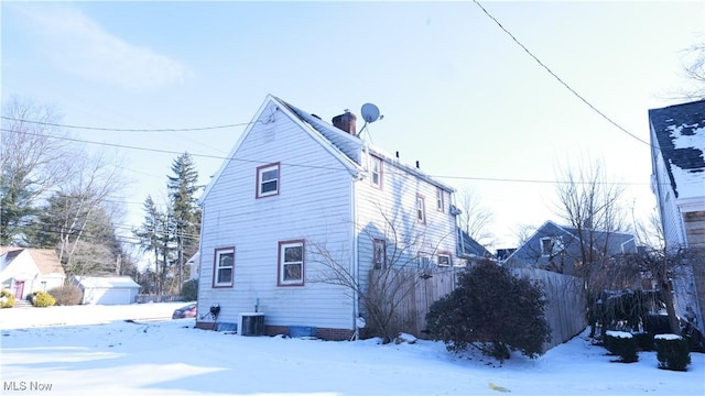 snow covered property with central AC and a chimney