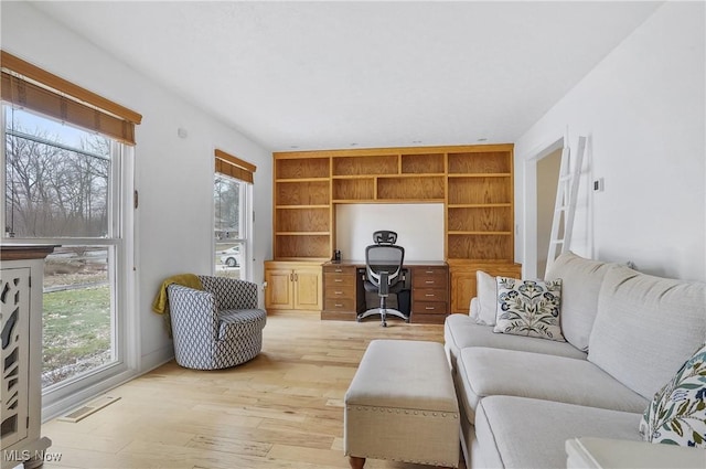 living room featuring built in features, plenty of natural light, and light hardwood / wood-style flooring