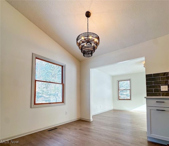 unfurnished dining area with a notable chandelier, light hardwood / wood-style flooring, a textured ceiling, and lofted ceiling