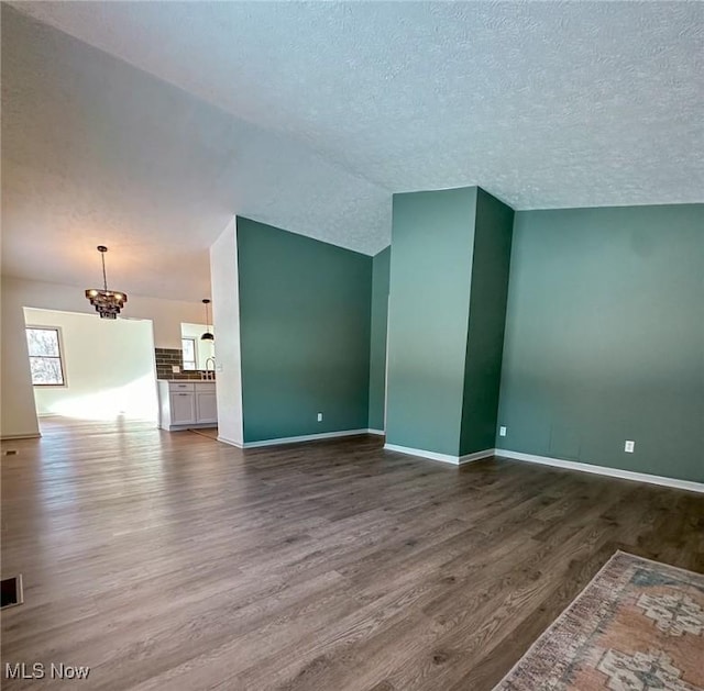 unfurnished living room with a chandelier, dark wood-type flooring, a textured ceiling, and lofted ceiling