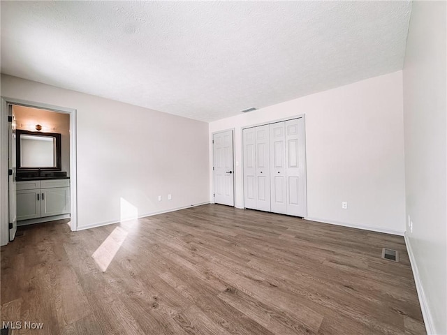 unfurnished bedroom featuring two closets, wood-type flooring, a textured ceiling, ensuite bathroom, and sink