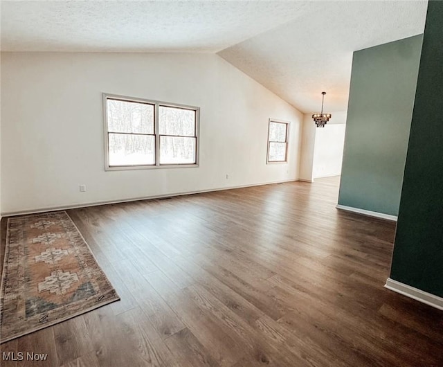 empty room featuring dark wood-type flooring, vaulted ceiling, an inviting chandelier, and a textured ceiling