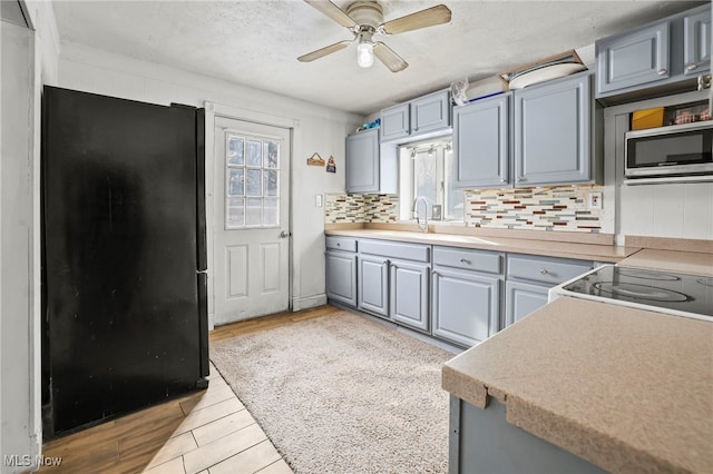 kitchen with gray cabinetry, black fridge, light hardwood / wood-style floors, ceiling fan, and decorative backsplash