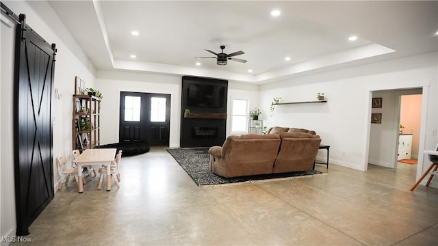 living room with a tray ceiling, a large fireplace, ceiling fan, and a barn door