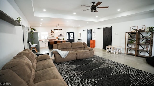 living room with concrete flooring, a raised ceiling, ceiling fan, and a barn door