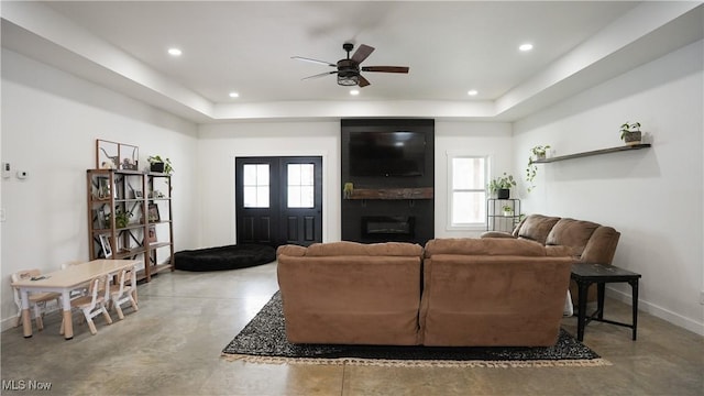 living room featuring a raised ceiling, ceiling fan, and a fireplace