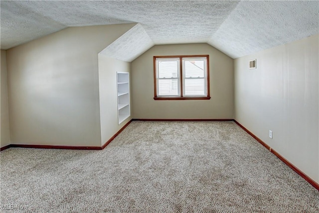 additional living space with lofted ceiling, a textured ceiling, light carpet, visible vents, and baseboards