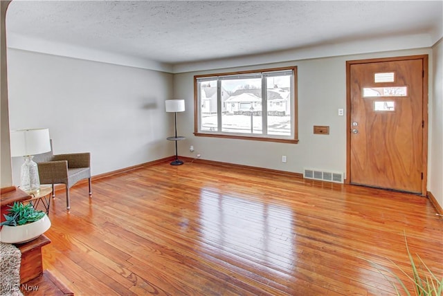 entryway with baseboards, light wood-style flooring, visible vents, and a textured ceiling