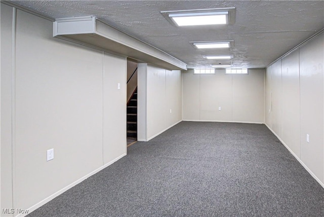 basement featuring stairway, dark colored carpet, and a textured ceiling