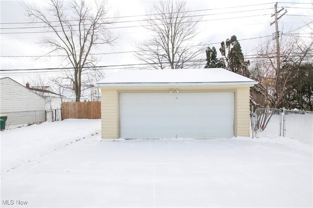 snow covered garage with a detached garage and fence