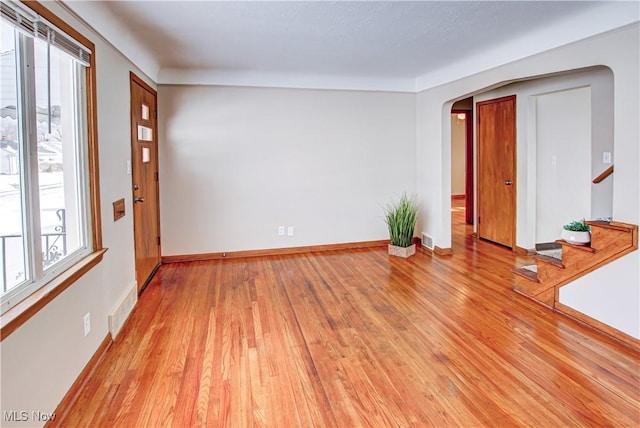 spare room with light wood-style floors, visible vents, and arched walkways