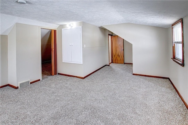 additional living space featuring visible vents, vaulted ceiling, a textured ceiling, and baseboards