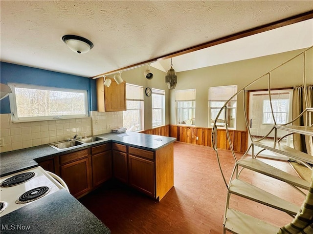 kitchen featuring a peninsula, brown cabinetry, dark countertops, and a sink