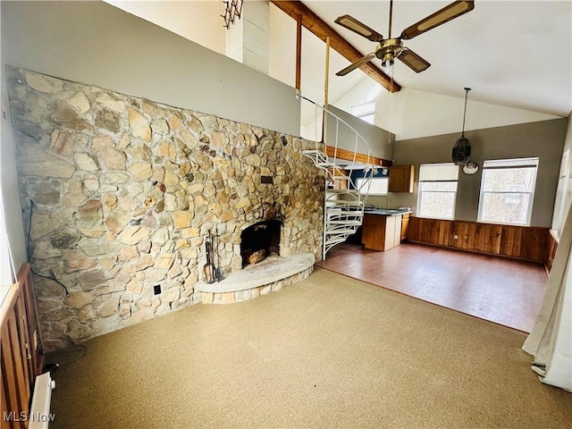 unfurnished living room with wooden walls, a ceiling fan, beamed ceiling, a fireplace, and high vaulted ceiling