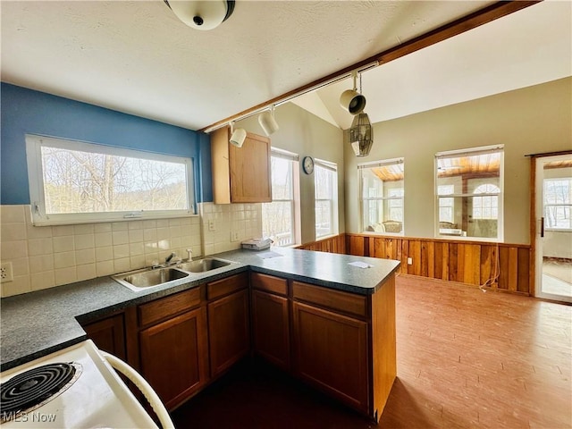 kitchen featuring brown cabinets, dark countertops, wainscoting, a sink, and a peninsula