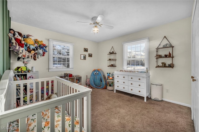 carpeted bedroom with a crib, ceiling fan, and a textured ceiling