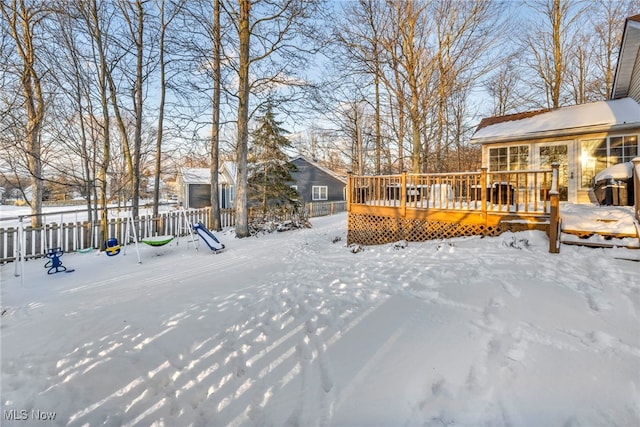 yard layered in snow featuring a playground and a wooden deck