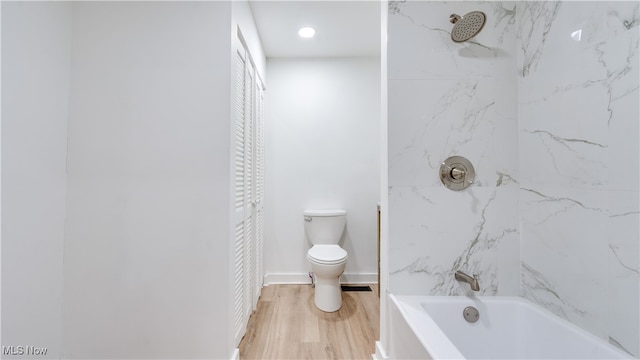 bathroom with wood-type flooring, tiled shower / bath, and toilet