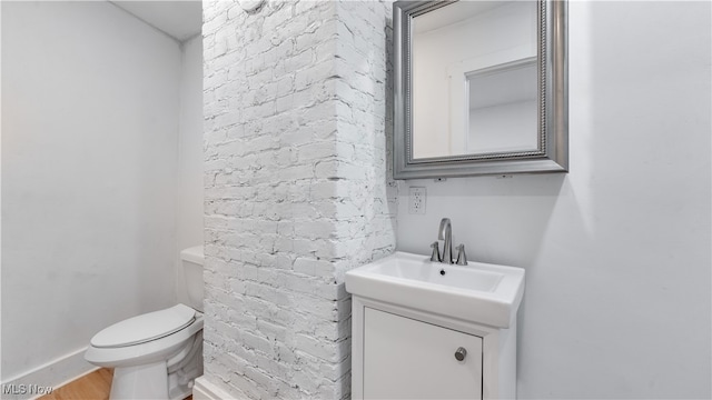 bathroom featuring toilet, vanity, and brick wall