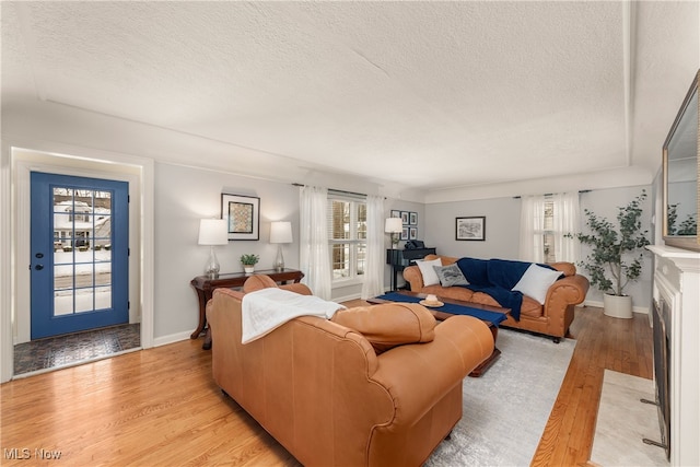 living room featuring a textured ceiling, baseboards, a fireplace with flush hearth, and light wood-style floors