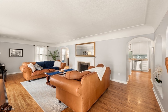 living room with light wood-style flooring, a fireplace, arched walkways, and baseboards