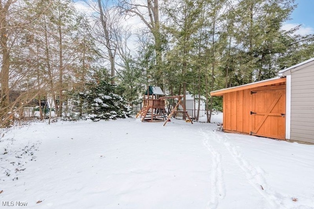 snowy yard featuring an outbuilding, a playground, and a storage shed