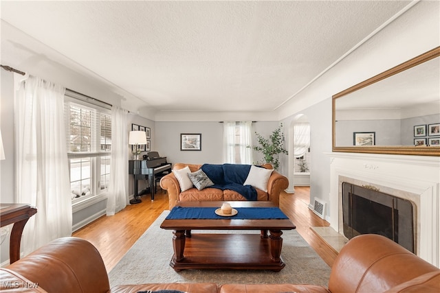 living area with a textured ceiling, a fireplace, visible vents, and wood finished floors