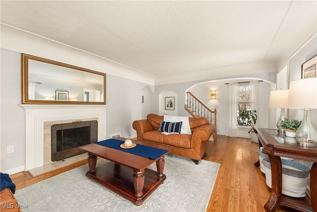 living area featuring arched walkways, a fireplace, visible vents, wood finished floors, and stairs