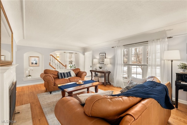 living area featuring light wood-style floors, arched walkways, a fireplace with flush hearth, and stairs