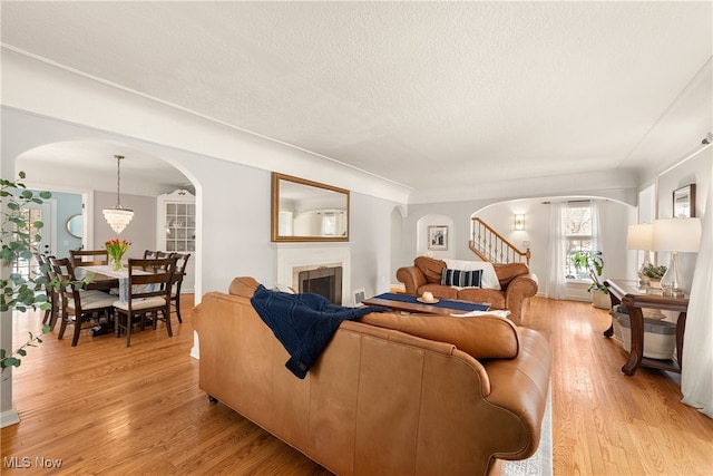 living room featuring arched walkways, light wood-type flooring, a fireplace, and a textured ceiling