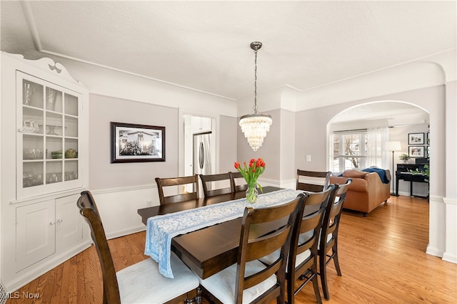 dining room with light wood-type flooring, arched walkways, and a notable chandelier