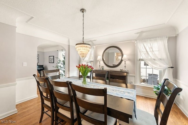 dining room featuring light wood-style floors, a wainscoted wall, a textured ceiling, and an inviting chandelier