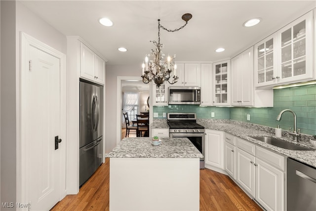 kitchen with stainless steel appliances, a sink, white cabinetry, light wood finished floors, and an inviting chandelier