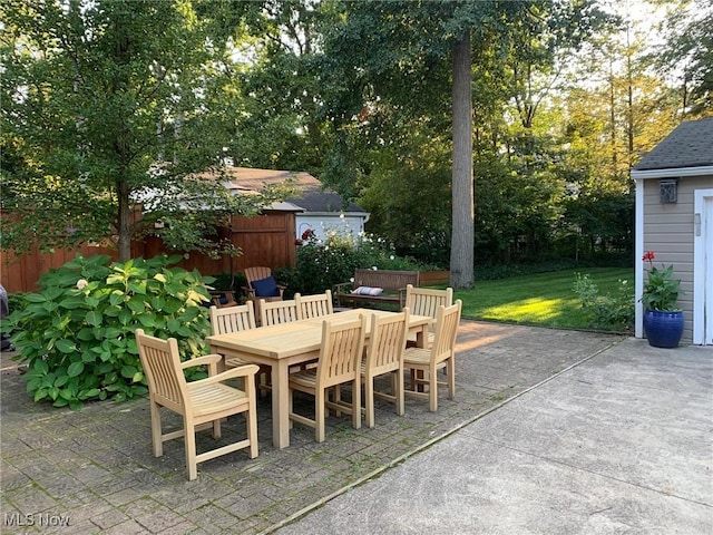 view of patio featuring outdoor dining space, fence, and an outbuilding