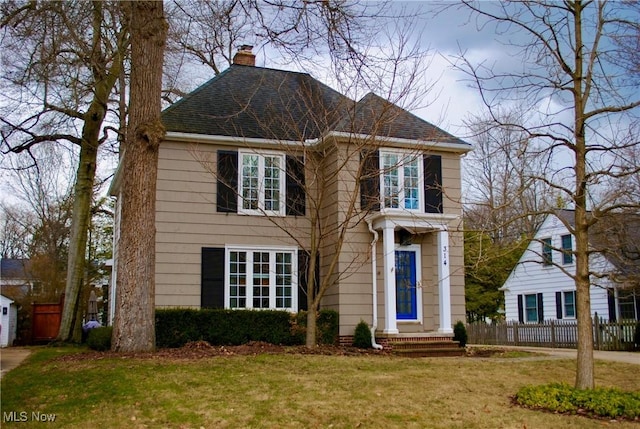 view of front of home featuring roof with shingles, a chimney, fence, and a front yard