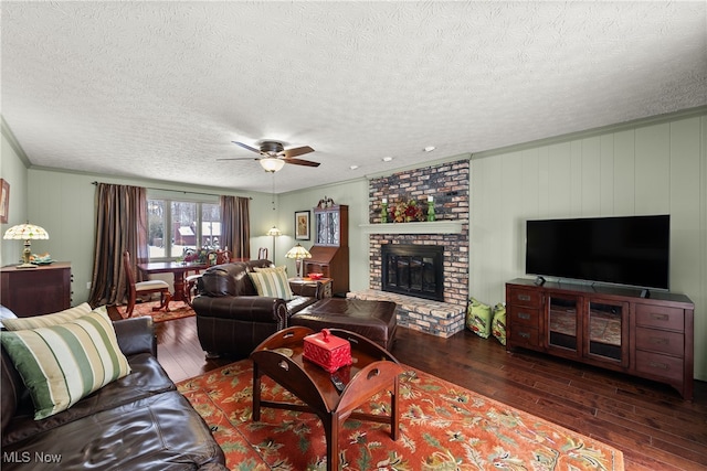 living room featuring a brick fireplace, dark wood-style flooring, ceiling fan, and a textured ceiling