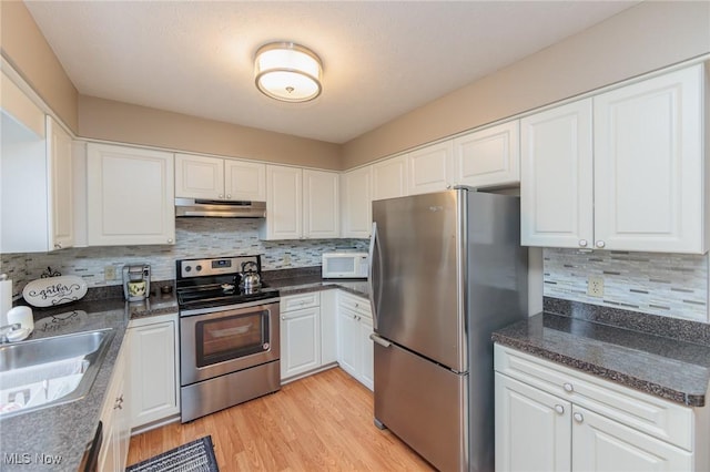 kitchen with under cabinet range hood, appliances with stainless steel finishes, white cabinets, dark countertops, and a sink