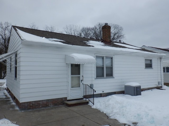 snow covered back of property featuring a chimney and entry steps