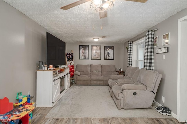 living room featuring ceiling fan, a textured ceiling, and light hardwood / wood-style floors