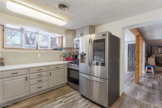 kitchen with stainless steel appliances, a textured ceiling, hardwood / wood-style flooring, and tasteful backsplash