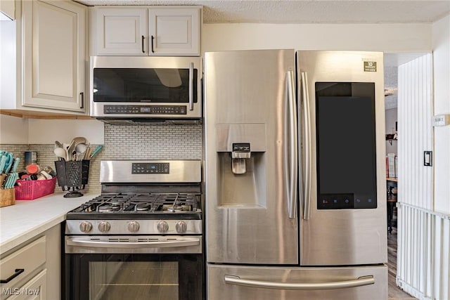 kitchen with stainless steel appliances, backsplash, cream cabinetry, and a textured ceiling