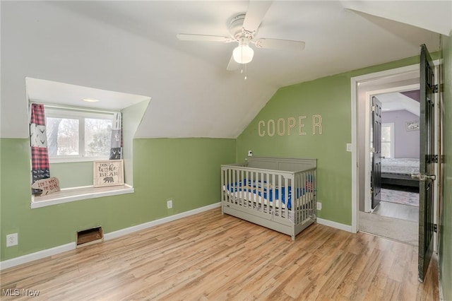 unfurnished bedroom featuring a nursery area, vaulted ceiling, light wood-type flooring, and ceiling fan