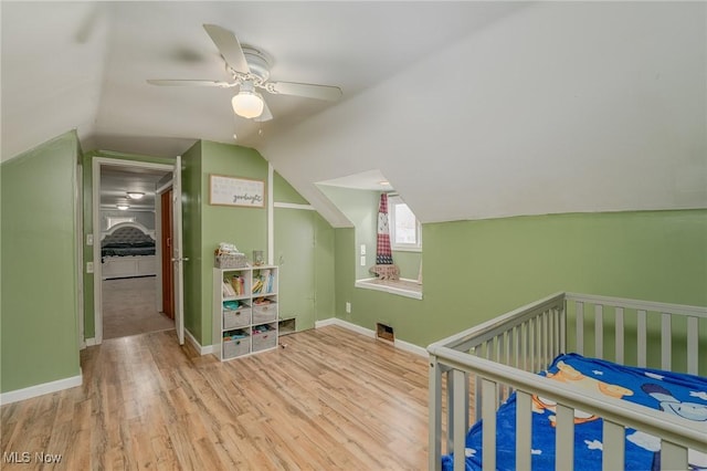 bedroom featuring a nursery area, light hardwood / wood-style flooring, lofted ceiling, and ceiling fan