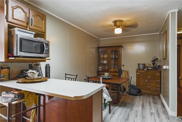 kitchen with kitchen peninsula, crown molding, a kitchen breakfast bar, and light hardwood / wood-style floors