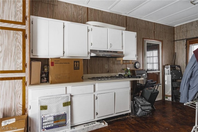 kitchen featuring white cabinetry, stainless steel gas stovetop, and wood walls