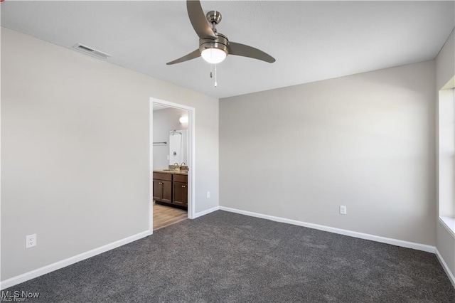 unfurnished bedroom with ensuite bath, baseboards, visible vents, and dark carpet