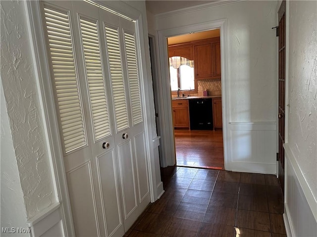 hall featuring a textured wall, a wainscoted wall, a sink, and a decorative wall